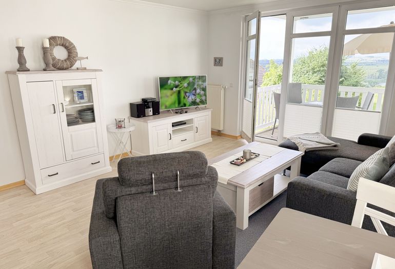 Wohnzimmer mit gemütlicher Couch, Couchtisch, Sessel sowie Smart-TV Wohnzimmer mit gemütlicher Couch, Couchtisch, Sessel sowie Smart-TV